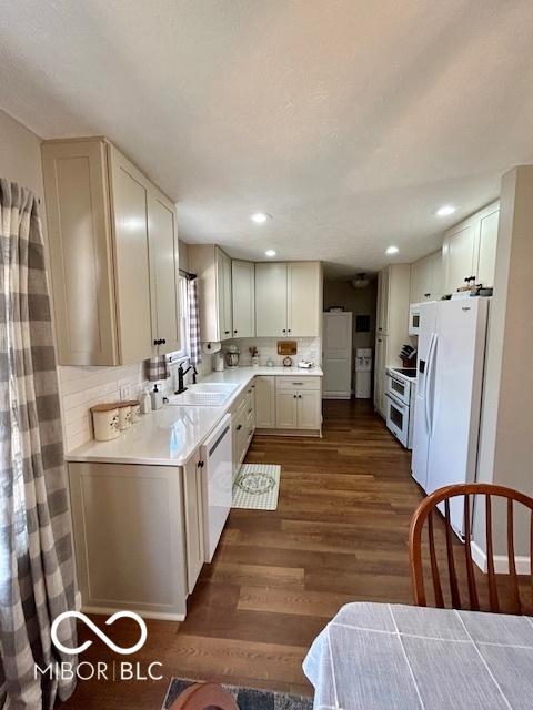 kitchen featuring a sink, tasteful backsplash, white appliances, light countertops, and dark wood-style flooring