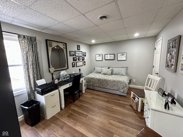 bedroom featuring visible vents, a drop ceiling, baseboards, and wood finished floors