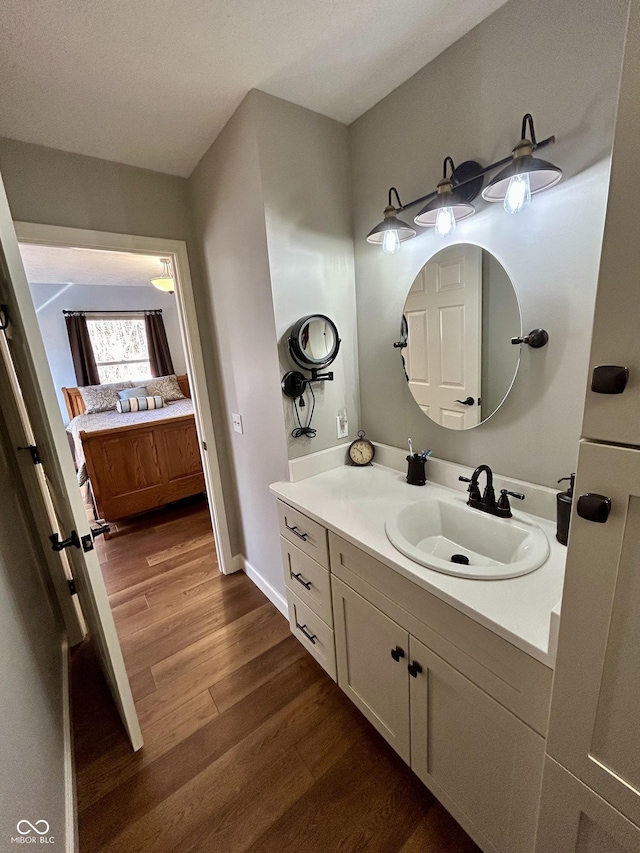 bathroom with ensuite bath, vanity, baseboards, and wood finished floors