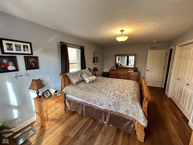 bedroom featuring baseboards, visible vents, dark wood-style flooring, a closet, and a textured ceiling