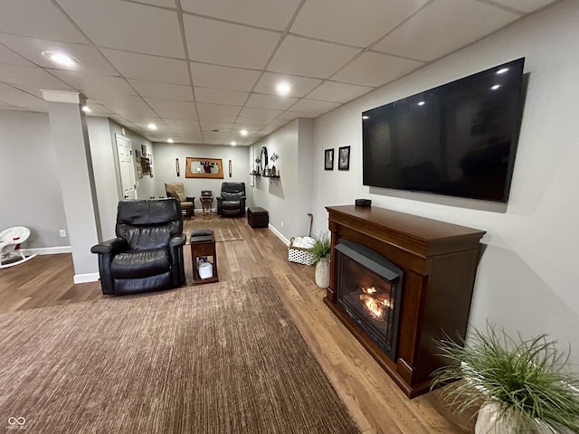 living room with a glass covered fireplace, wood finished floors, baseboards, and a drop ceiling