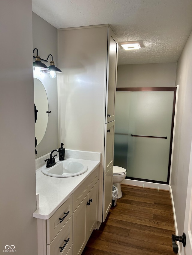 bathroom featuring toilet, vanity, a stall shower, wood finished floors, and a textured ceiling