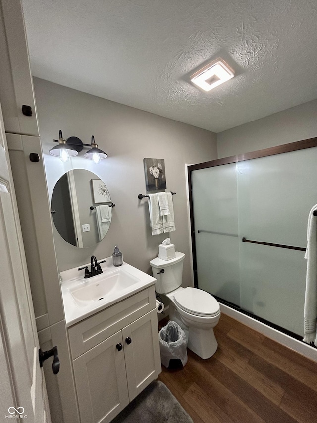 bathroom featuring toilet, a stall shower, a textured ceiling, wood finished floors, and vanity