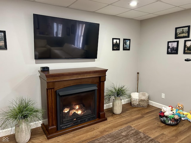 interior space featuring a drop ceiling, baseboards, a warm lit fireplace, and wood finished floors