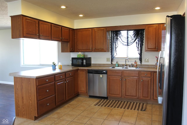 kitchen with brown cabinets, appliances with stainless steel finishes, a peninsula, and a sink