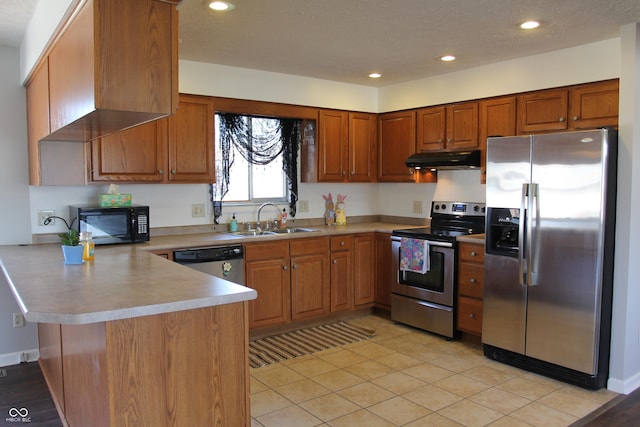 kitchen featuring brown cabinets, under cabinet range hood, a sink, stainless steel appliances, and a peninsula