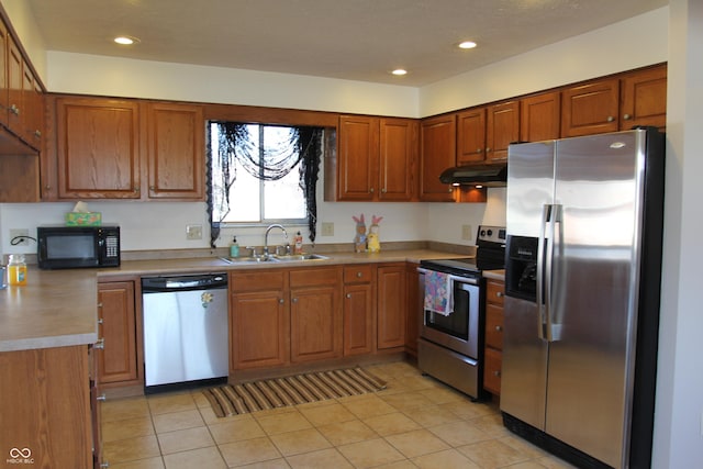 kitchen with under cabinet range hood, brown cabinets, appliances with stainless steel finishes, and a sink