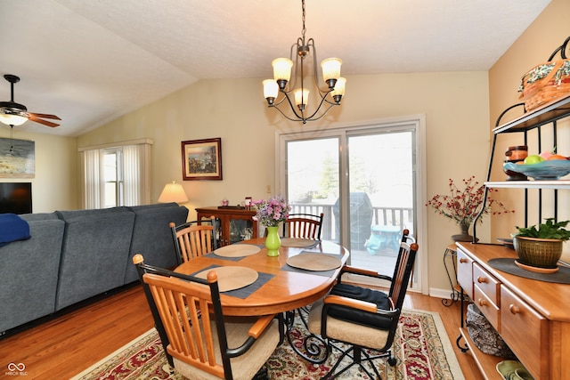 dining area featuring ceiling fan with notable chandelier, light wood-style floors, and vaulted ceiling