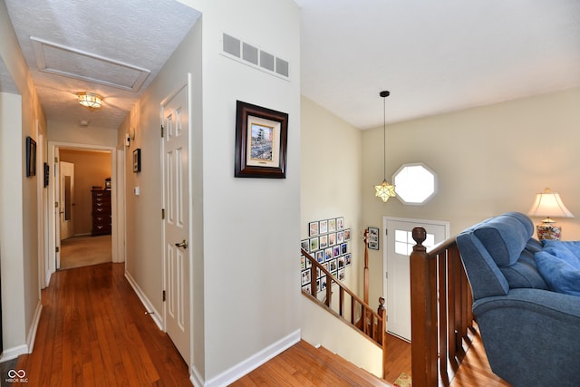 hall with visible vents, an upstairs landing, wood finished floors, baseboards, and attic access