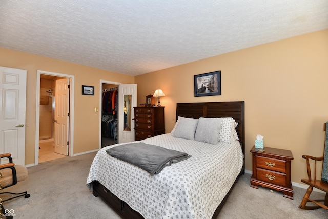 bedroom featuring a spacious closet, baseboards, light colored carpet, a closet, and a textured ceiling