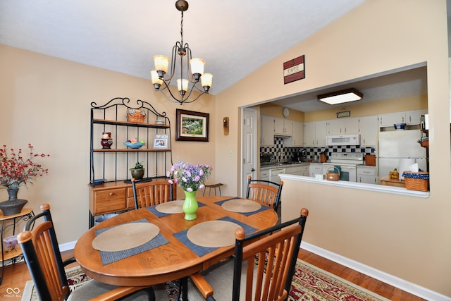 dining space with a chandelier, baseboards, lofted ceiling, and wood finished floors