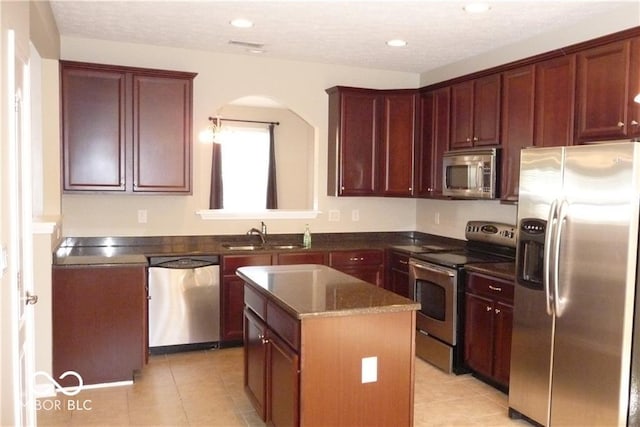 kitchen with light tile patterned floors, a sink, appliances with stainless steel finishes, reddish brown cabinets, and a center island