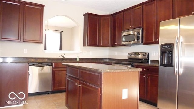 kitchen featuring light tile patterned floors, a kitchen island, arched walkways, dark brown cabinets, and appliances with stainless steel finishes