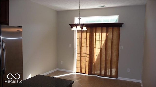 unfurnished dining area featuring an inviting chandelier, baseboards, visible vents, and a textured ceiling