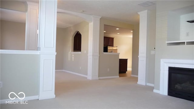 unfurnished living room with light carpet, a glass covered fireplace, recessed lighting, baseboards, and ornate columns