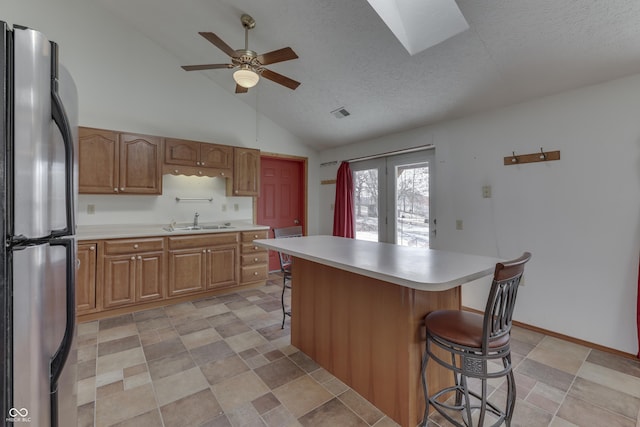 kitchen with brown cabinets, a sink, freestanding refrigerator, a breakfast bar area, and light countertops