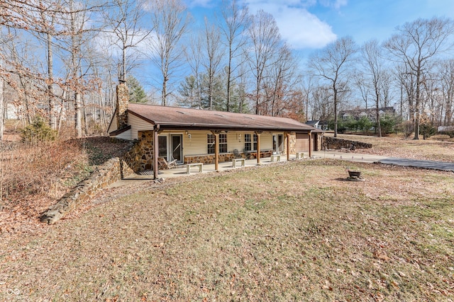 back of house featuring a patio area, stone siding, a lawn, and a chimney