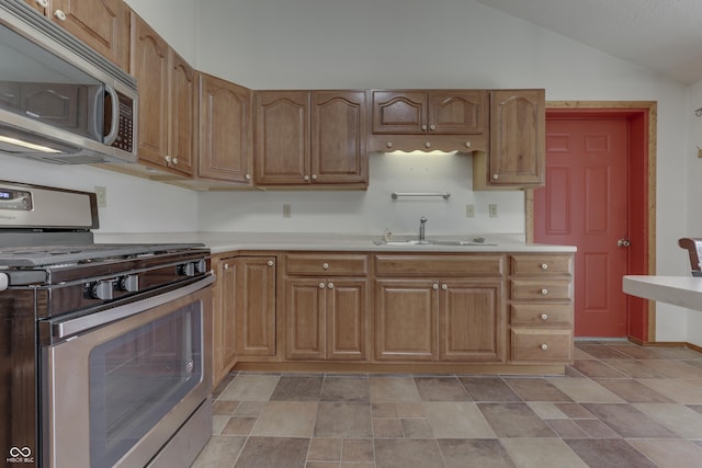 kitchen featuring light countertops, vaulted ceiling, brown cabinets, stainless steel appliances, and a sink