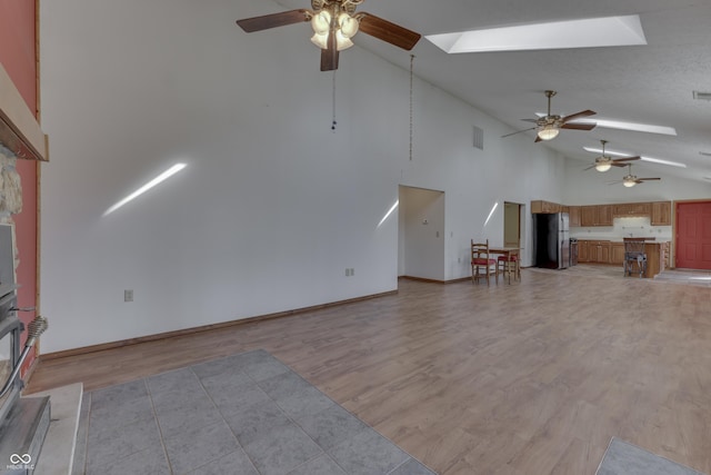 unfurnished living room featuring a skylight, visible vents, light wood-type flooring, and high vaulted ceiling