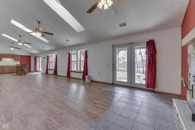 unfurnished living room with vaulted ceiling with skylight, visible vents, a healthy amount of sunlight, and light wood-style floors