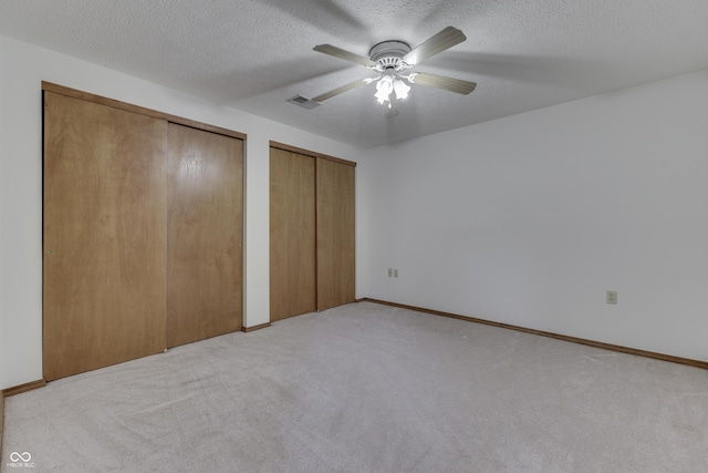 unfurnished bedroom featuring visible vents, ceiling fan, a textured ceiling, light carpet, and two closets