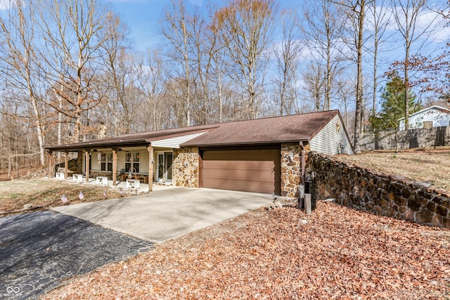 view of front facade featuring stone siding, driveway, an attached garage, and roof with shingles