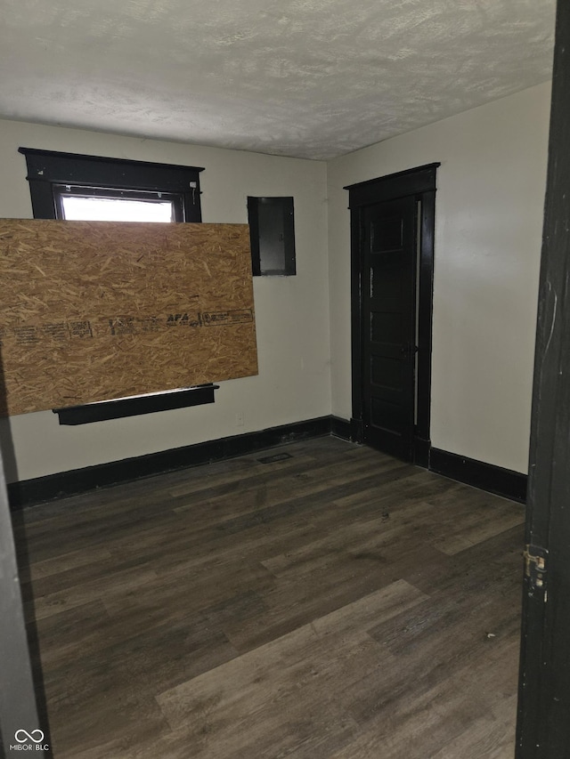 spare room with electric panel, baseboards, and dark wood-type flooring