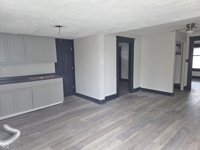 unfurnished living room with ceiling fan, baseboards, light wood-type flooring, and a textured ceiling