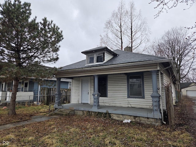 bungalow with a porch, fence, roof with shingles, and a chimney