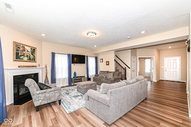 living area with light wood-type flooring, visible vents, a glass covered fireplace, and stairs