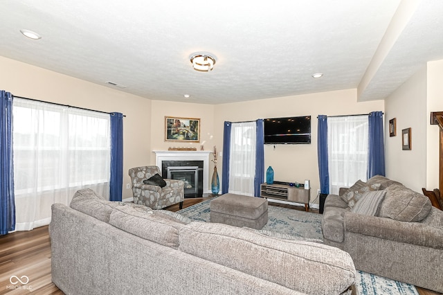 living room with a glass covered fireplace, a textured ceiling, visible vents, and wood finished floors