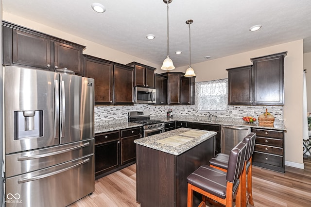 kitchen with a kitchen island, a sink, stainless steel appliances, dark brown cabinetry, and tasteful backsplash