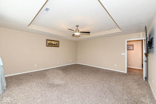 empty room featuring a raised ceiling, light carpet, visible vents, and ceiling fan