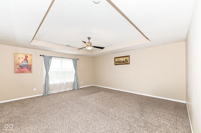 carpeted spare room with a tray ceiling, a ceiling fan, and baseboards