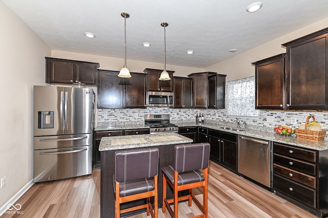 kitchen with a kitchen island, light wood-style flooring, a sink, dark brown cabinets, and appliances with stainless steel finishes