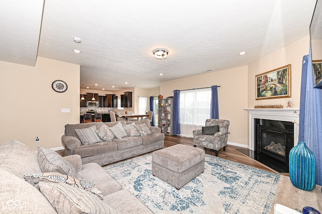 living room featuring a glass covered fireplace, baseboards, wood finished floors, and recessed lighting