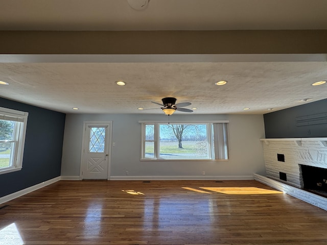 unfurnished living room with a stone fireplace, plenty of natural light, baseboards, and wood finished floors