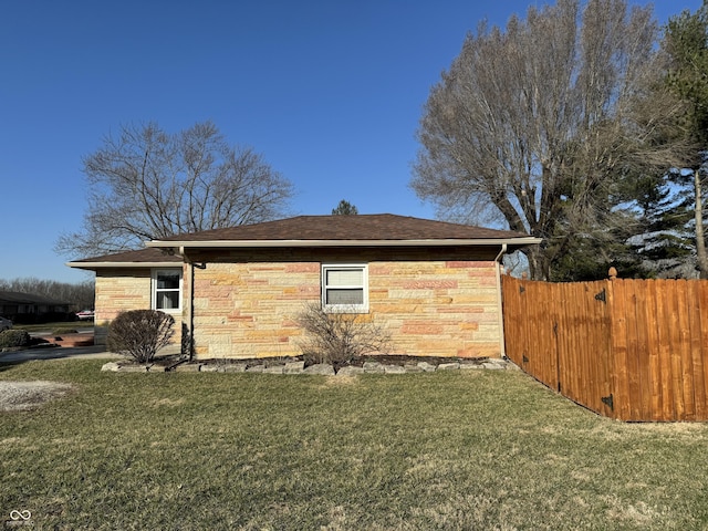 view of side of home with a yard, stone siding, and fence