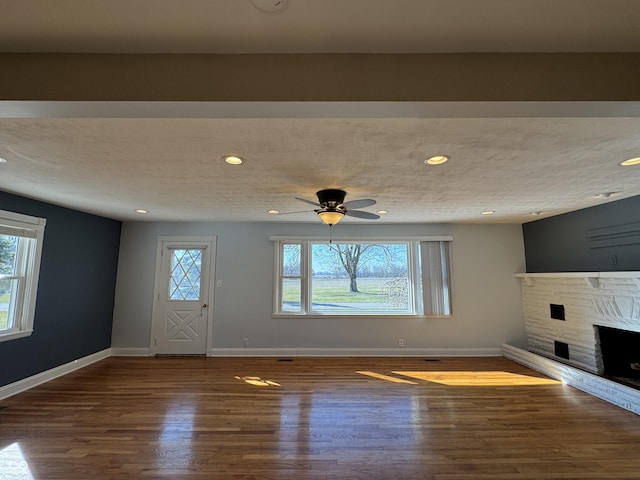 unfurnished living room featuring a stone fireplace, recessed lighting, baseboards, and wood finished floors