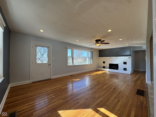 unfurnished living room with visible vents, wood finished floors, baseboards, and a fireplace with raised hearth