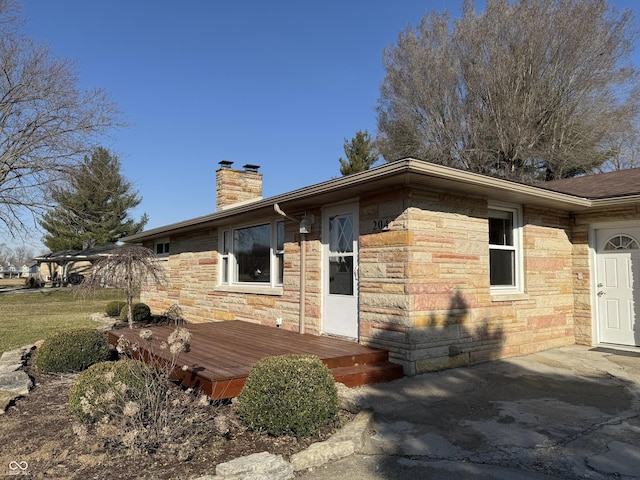 view of front of home featuring a wooden deck, stone siding, and a chimney