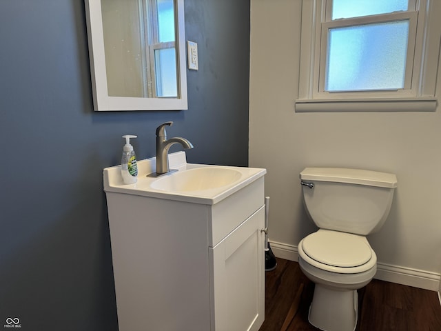 half bath featuring vanity, toilet, wood finished floors, and baseboards