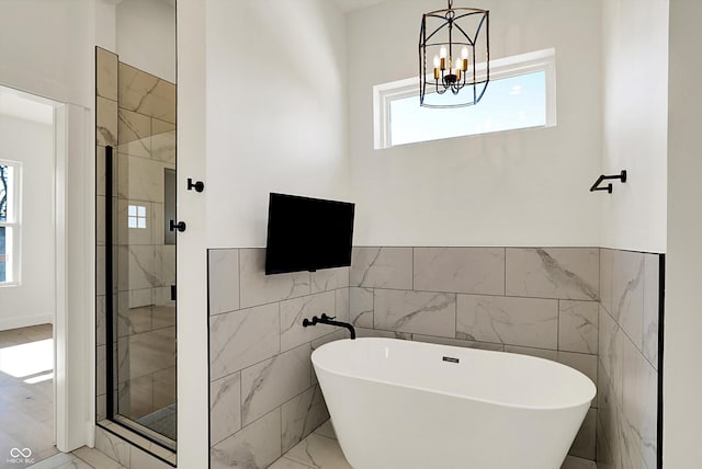 full bath featuring a freestanding bath, a stall shower, a notable chandelier, marble finish floor, and tile walls