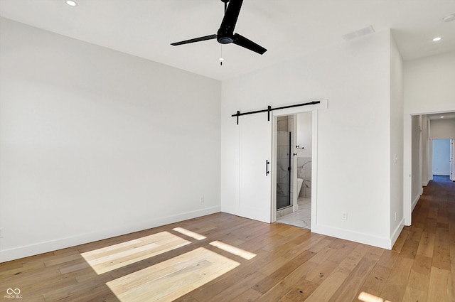 unfurnished bedroom with baseboards, recessed lighting, light wood-style floors, a barn door, and connected bathroom