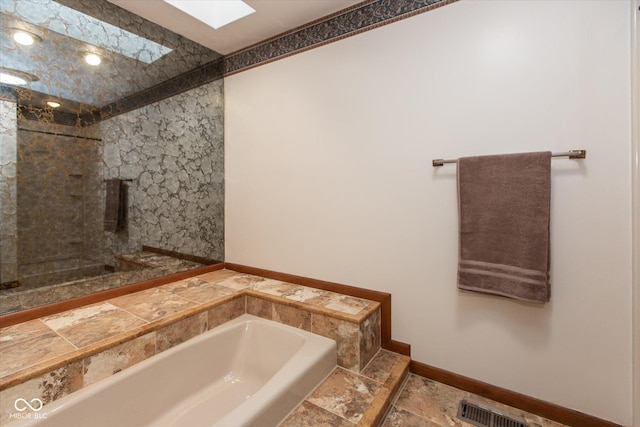 full bath with visible vents, a skylight, a stall shower, stone tile flooring, and a bath