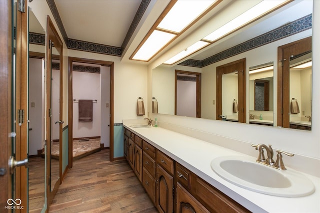 full bathroom with a sink, baseboards, wood finished floors, and double vanity