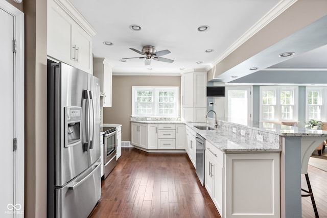 kitchen with a peninsula, ornamental molding, white cabinets, appliances with stainless steel finishes, and a kitchen breakfast bar