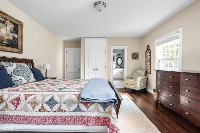 bedroom featuring a closet, connected bathroom, baseboards, and dark wood-style flooring