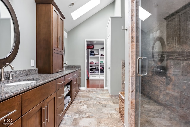 full bathroom with vanity, a shower stall, a spacious closet, stone finish flooring, and lofted ceiling with skylight