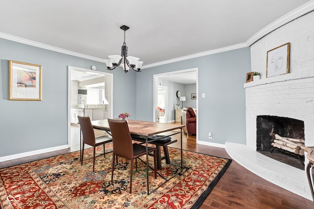 dining room with dark wood-type flooring, an inviting chandelier, a fireplace, crown molding, and baseboards